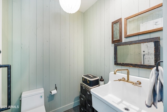 bathroom featuring a sink, toilet, and wooden walls