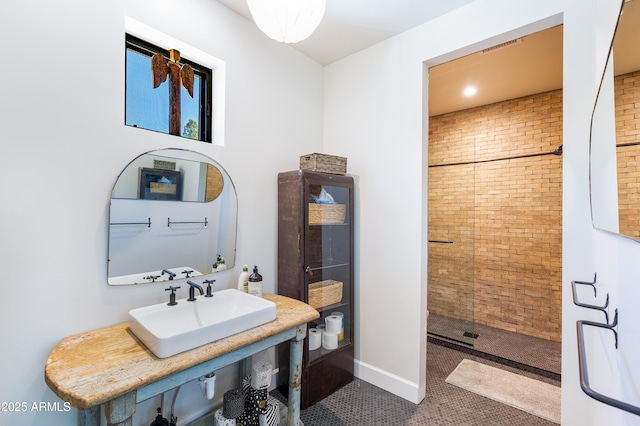 bathroom with tile patterned flooring, brick wall, baseboards, tiled shower, and a sink