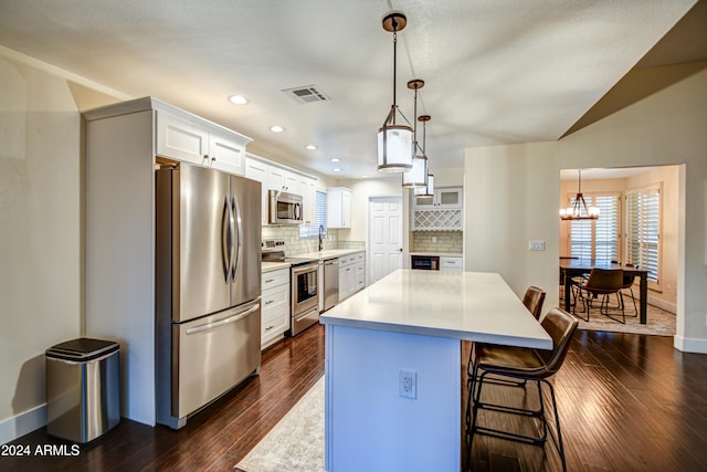 kitchen with white cabinets, appliances with stainless steel finishes, pendant lighting, and dark wood-type flooring