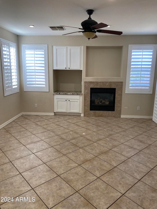 unfurnished living room with a tiled fireplace, light tile patterned floors, and ceiling fan