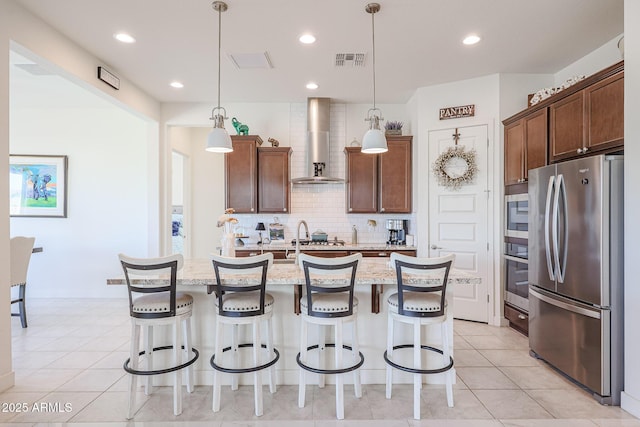 kitchen featuring stainless steel appliances, a kitchen island with sink, hanging light fixtures, and wall chimney range hood