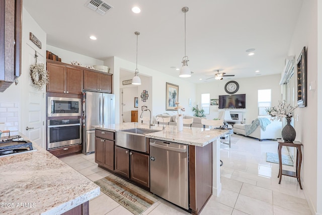 kitchen with appliances with stainless steel finishes, pendant lighting, an island with sink, sink, and light stone counters