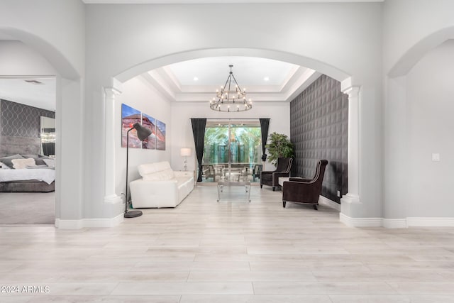 living area with light wood-type flooring, a raised ceiling, a chandelier, and ornate columns