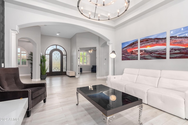 living room featuring a raised ceiling, decorative columns, ceiling fan with notable chandelier, and light hardwood / wood-style flooring