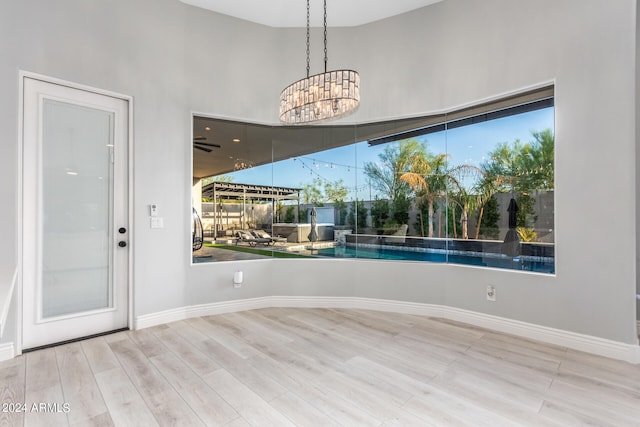 unfurnished room with an inviting chandelier, plenty of natural light, light hardwood / wood-style floors, and a high ceiling