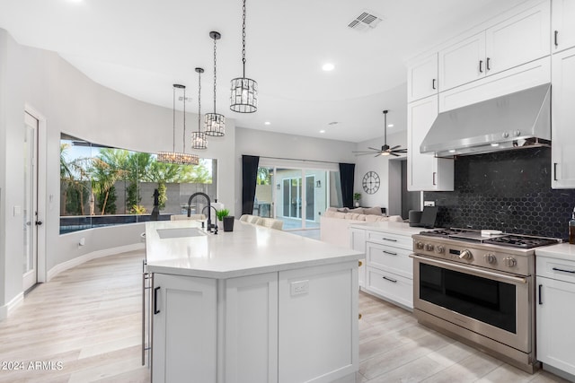 kitchen featuring ventilation hood, light wood-type flooring, a center island with sink, sink, and stainless steel range