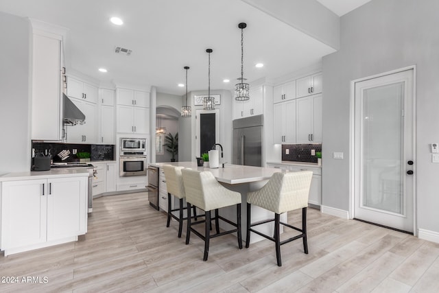 kitchen with white cabinets, an island with sink, backsplash, built in appliances, and light hardwood / wood-style floors