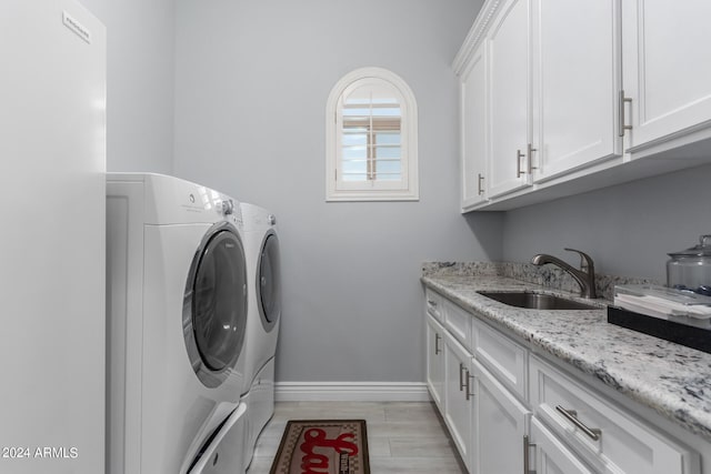 clothes washing area with light hardwood / wood-style floors, separate washer and dryer, sink, and cabinets