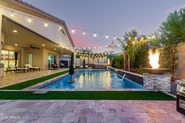 pool at dusk with pool water feature, ceiling fan, and a patio area