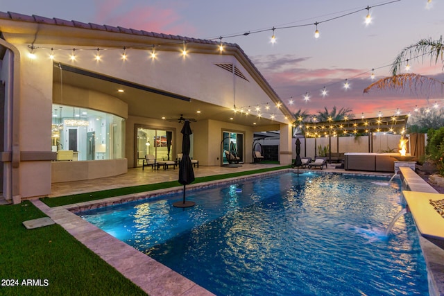 pool at dusk with a patio, outdoor lounge area, ceiling fan, a hot tub, and pool water feature