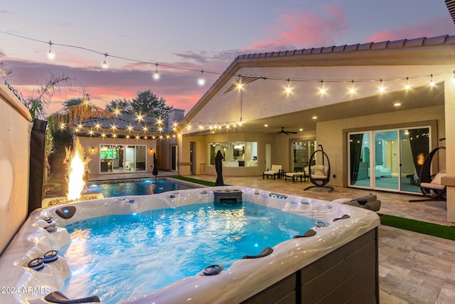 pool at dusk with ceiling fan, a patio area, and a hot tub