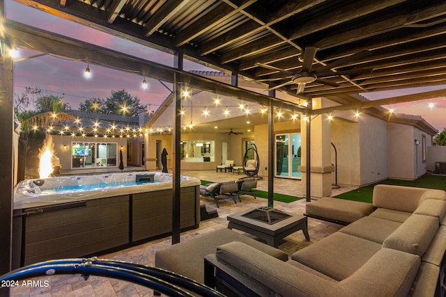 patio terrace at dusk with a hot tub, an outdoor living space with a fire pit, and ceiling fan