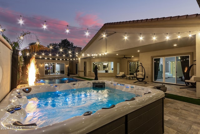 pool at dusk with a hot tub, ceiling fan, and a patio