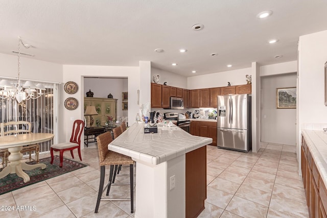 kitchen featuring kitchen peninsula, appliances with stainless steel finishes, a breakfast bar, tile countertops, and hanging light fixtures