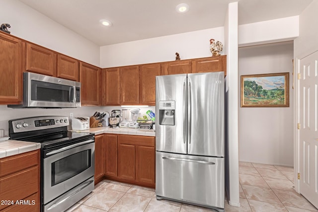 kitchen with tile counters, light tile patterned flooring, and stainless steel appliances