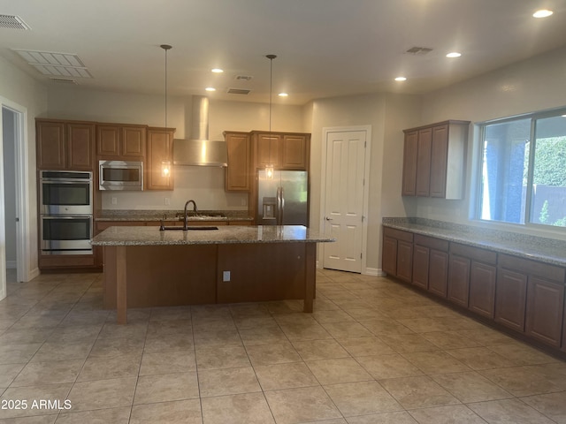 kitchen with pendant lighting, an island with sink, sink, stainless steel appliances, and wall chimney exhaust hood