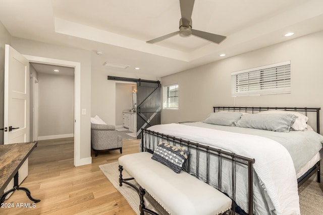 bedroom with light hardwood / wood-style floors, a raised ceiling, a barn door, and ceiling fan