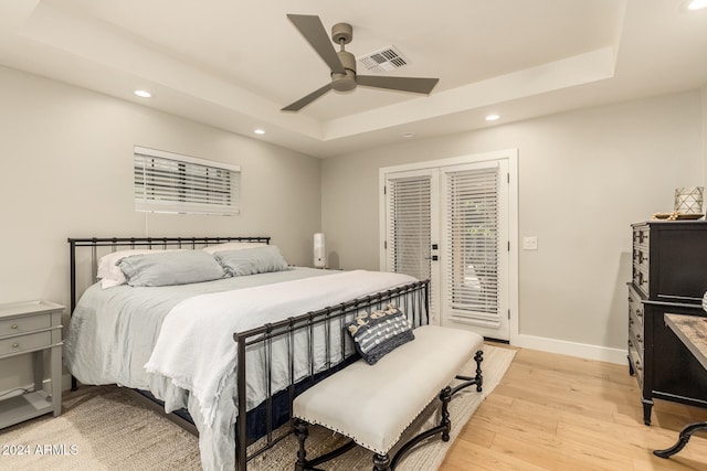 bedroom featuring ceiling fan, a tray ceiling, light wood-type flooring, and access to exterior