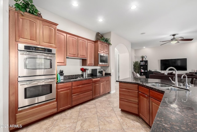 kitchen with appliances with stainless steel finishes, ceiling fan, sink, and dark stone countertops