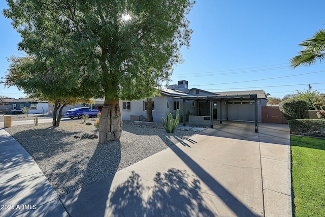 view of front of house featuring a garage, solar panels, concrete driveway, and fence