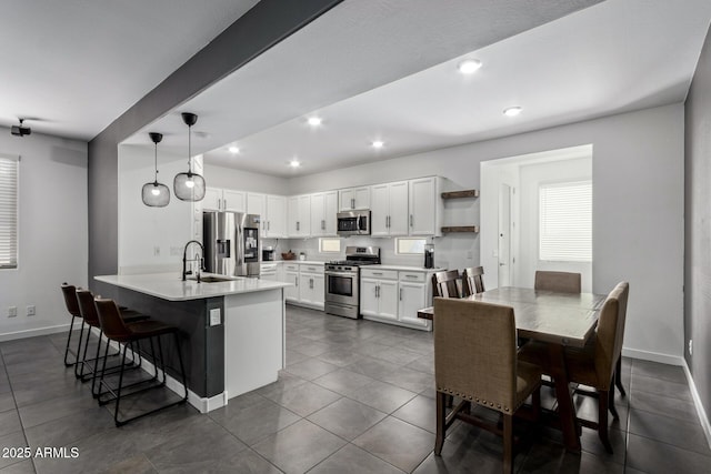 kitchen featuring a breakfast bar, appliances with stainless steel finishes, white cabinetry, decorative light fixtures, and kitchen peninsula