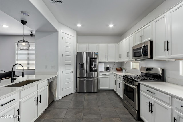 kitchen featuring sink, appliances with stainless steel finishes, dark tile patterned flooring, pendant lighting, and white cabinets