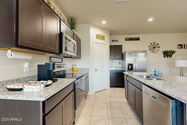 kitchen with dark brown cabinetry, sink, light tile patterned floors, stainless steel appliances, and a kitchen island with sink