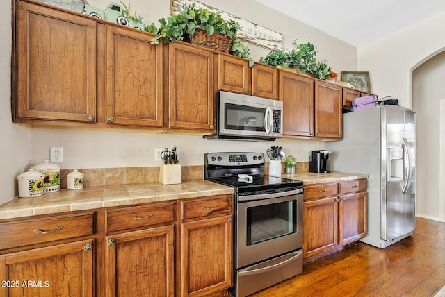 kitchen with dark wood-type flooring, appliances with stainless steel finishes, and tile counters