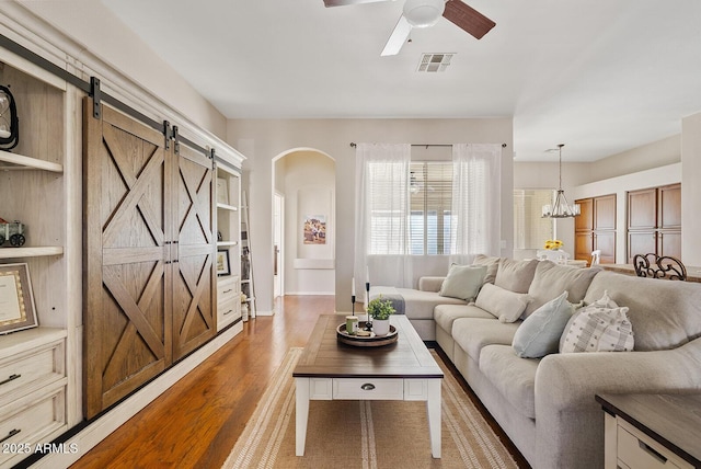 living room featuring a barn door, ceiling fan with notable chandelier, and light wood-type flooring