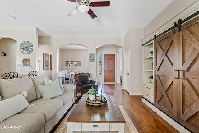 living room featuring a barn door, ceiling fan with notable chandelier, and dark hardwood / wood-style flooring