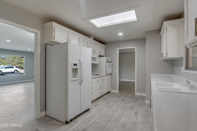 kitchen featuring white appliances, white cabinetry, light wood-style floors, and a sink