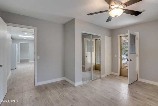 unfurnished bedroom featuring visible vents, baseboards, freestanding refrigerator, light wood finished floors, and two closets