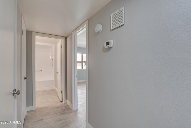 hallway with baseboards, visible vents, and light wood-style floors