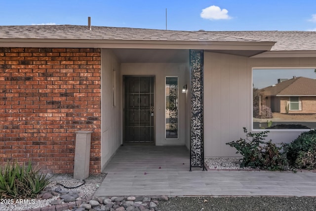 entrance to property featuring a shingled roof and brick siding