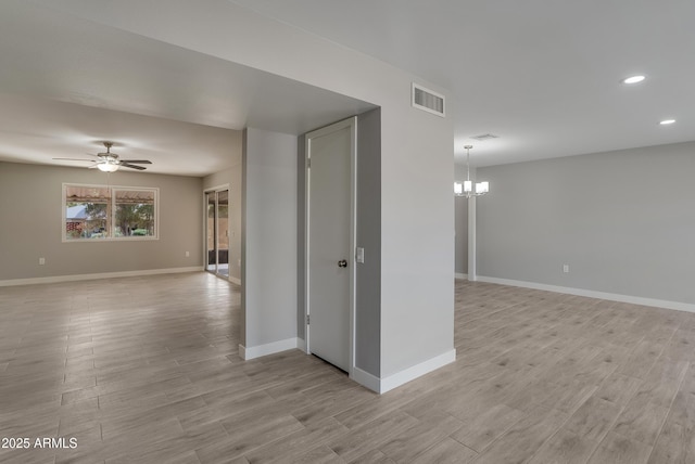 spare room featuring light wood-type flooring, baseboards, visible vents, and ceiling fan with notable chandelier