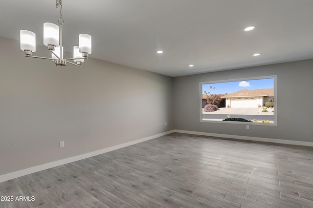 unfurnished room with a notable chandelier, recessed lighting, wood finished floors, and baseboards