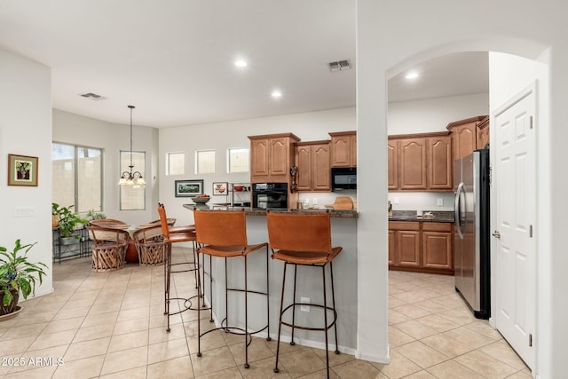 kitchen featuring a center island with sink, dark stone countertops, a breakfast bar area, and black appliances