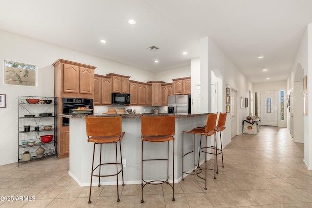 kitchen featuring a center island, dark stone counters, a breakfast bar, and black appliances