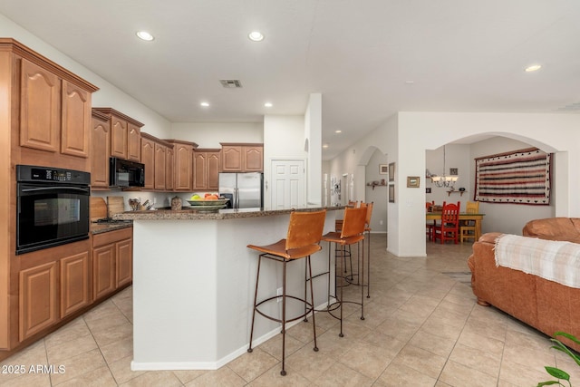 kitchen with light tile patterned flooring, a breakfast bar area, a center island, dark stone countertops, and black appliances