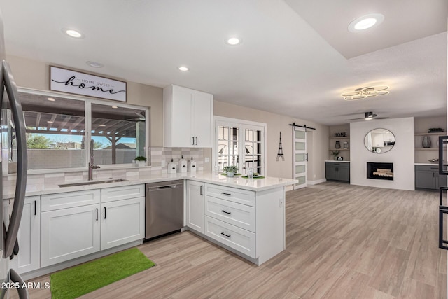 kitchen with stainless steel appliances, a barn door, white cabinets, a sink, and a peninsula