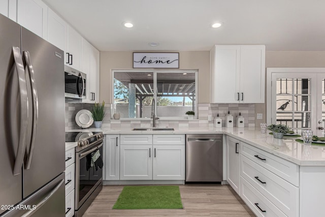 kitchen featuring light stone counters, stainless steel appliances, backsplash, white cabinetry, and a sink