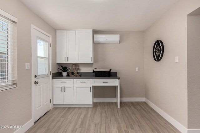 kitchen featuring light wood finished floors, baseboards, white cabinets, dark countertops, and a wall unit AC