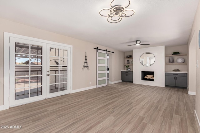 unfurnished living room featuring light wood finished floors, a barn door, a fireplace, and a ceiling fan