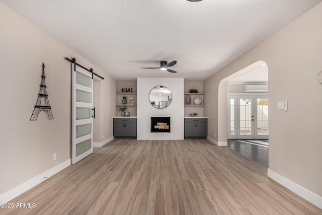 unfurnished living room with arched walkways, a fireplace, light wood-style flooring, a barn door, and a wall mounted AC