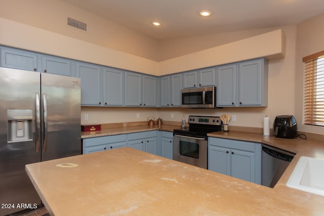 kitchen featuring sink, kitchen peninsula, appliances with stainless steel finishes, blue cabinetry, and lofted ceiling