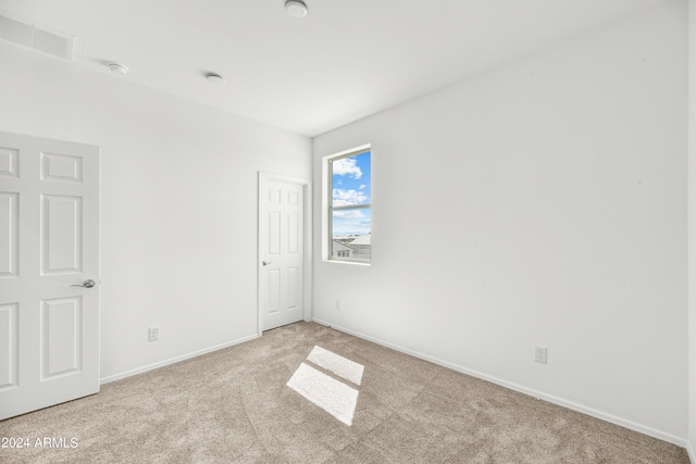 spare room featuring light carpet, baseboards, and a smoke detector