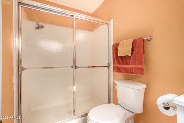 bathroom featuring a shower with door and toilet