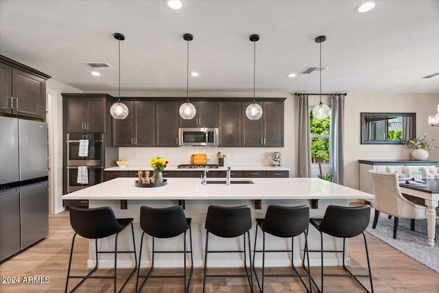 kitchen featuring light hardwood / wood-style floors, a center island with sink, hanging light fixtures, and appliances with stainless steel finishes