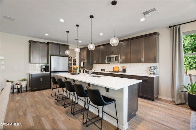 kitchen featuring appliances with stainless steel finishes, light hardwood / wood-style floors, hanging light fixtures, and sink