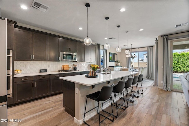 kitchen featuring hanging light fixtures, stainless steel appliances, plenty of natural light, and an island with sink